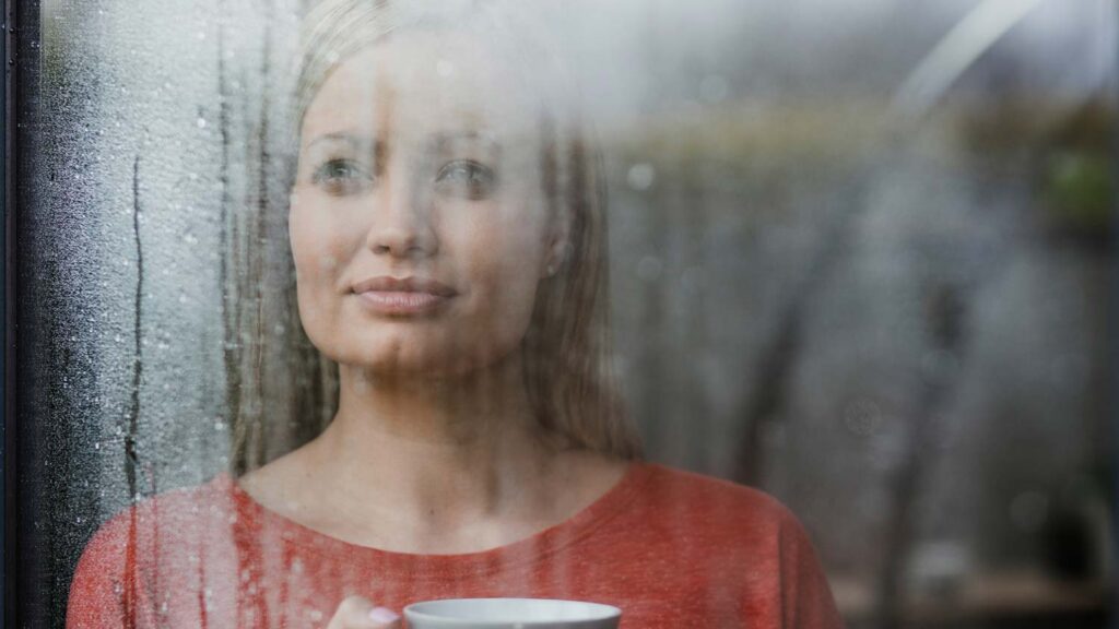 woman looking out window with coffee