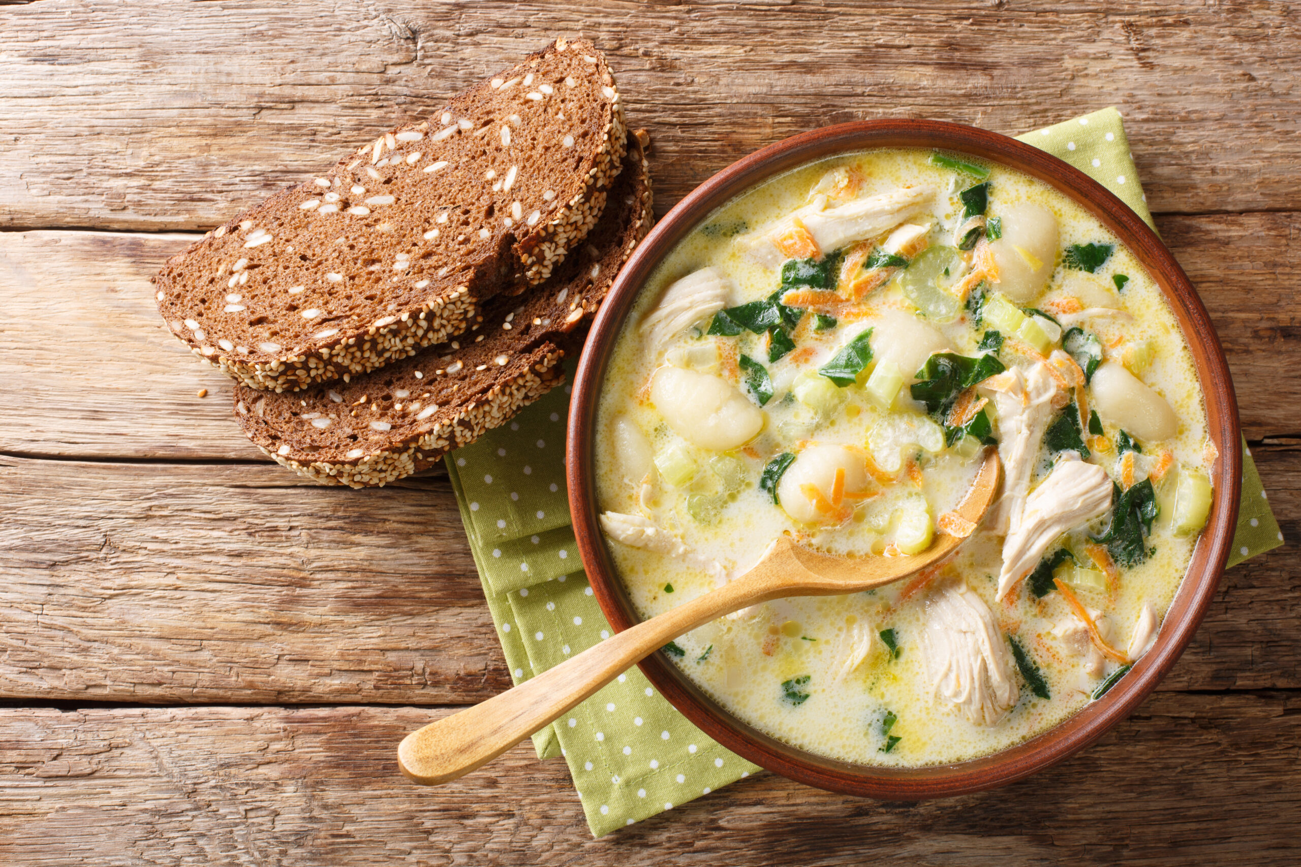 Homemade Italian cream soup with gnocchi, chicken and spinach served with bread close-up in a bowl. Horizontal top view