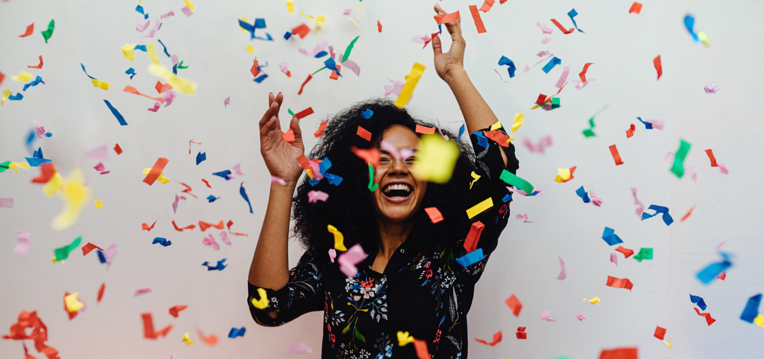 Young woman dancing under confetti at home, celebrating birthday