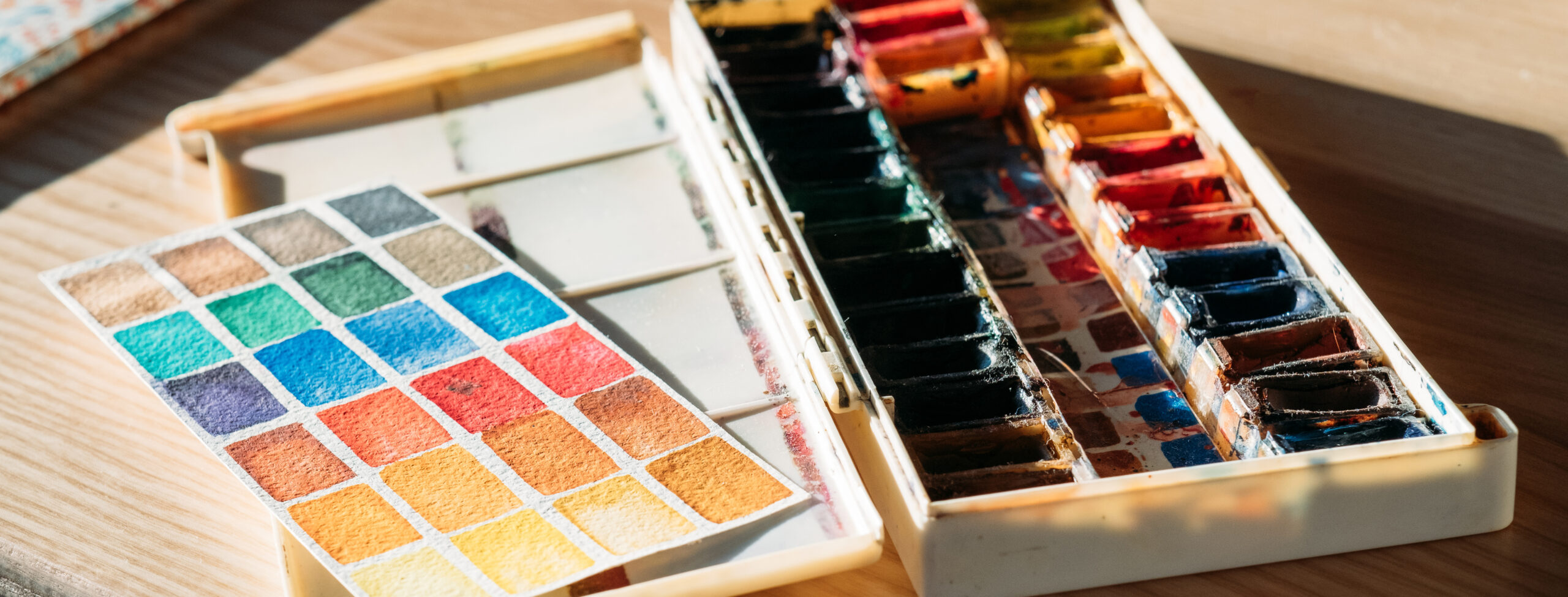 Art supplies at workplace. Artist tools. Watercolor paint set and color chart on desk.