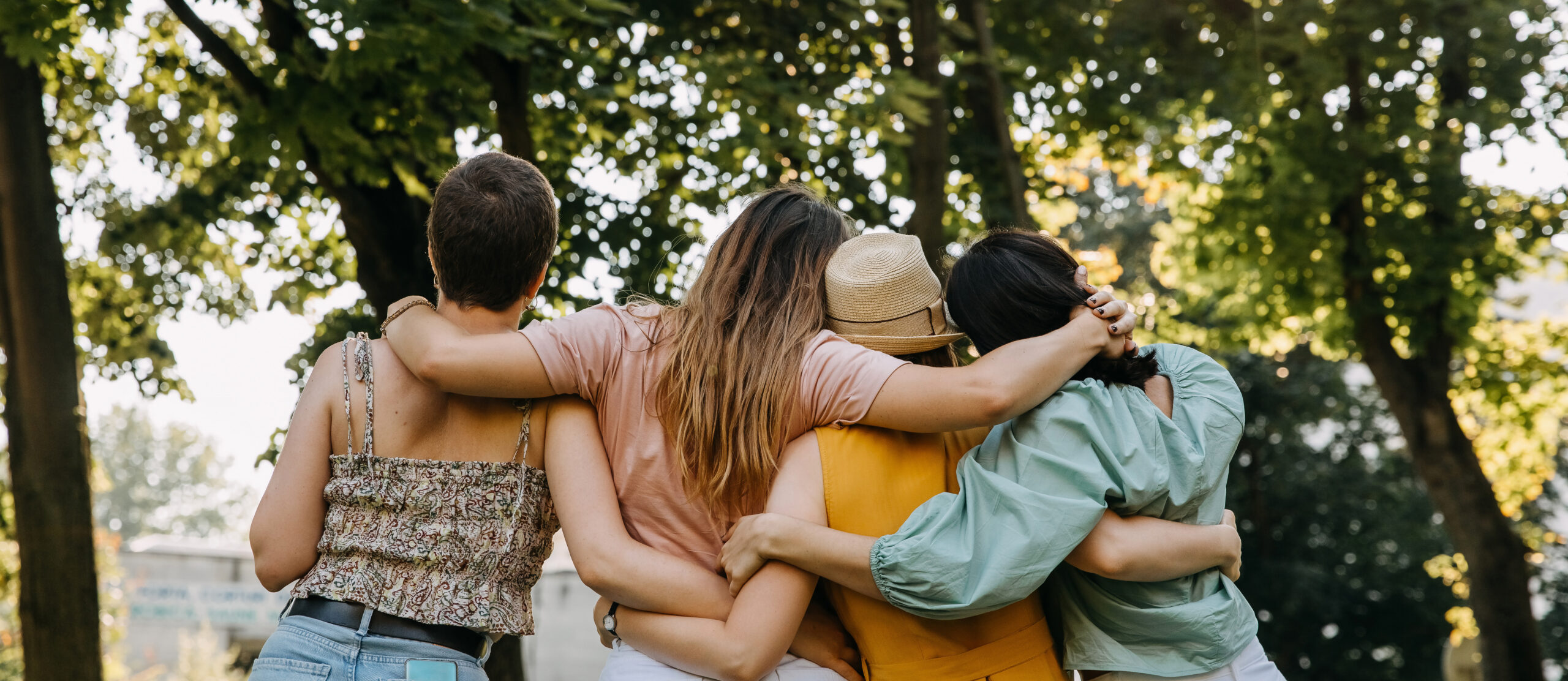 Group of four women in a park, hugging together from behind.